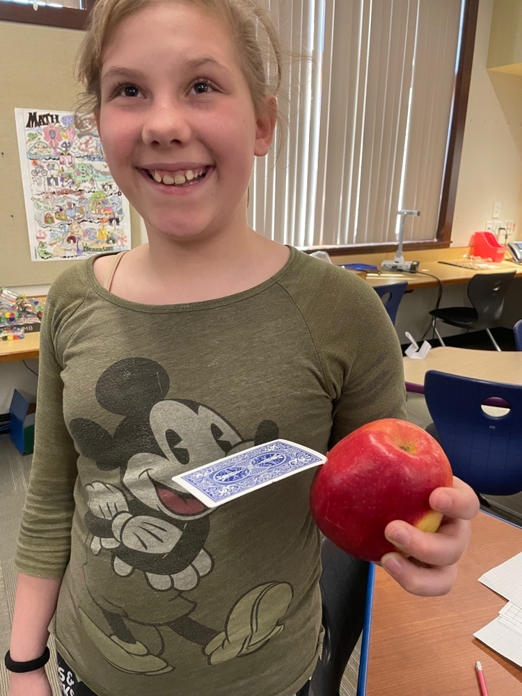Student holding a card with an apple stuck in it.