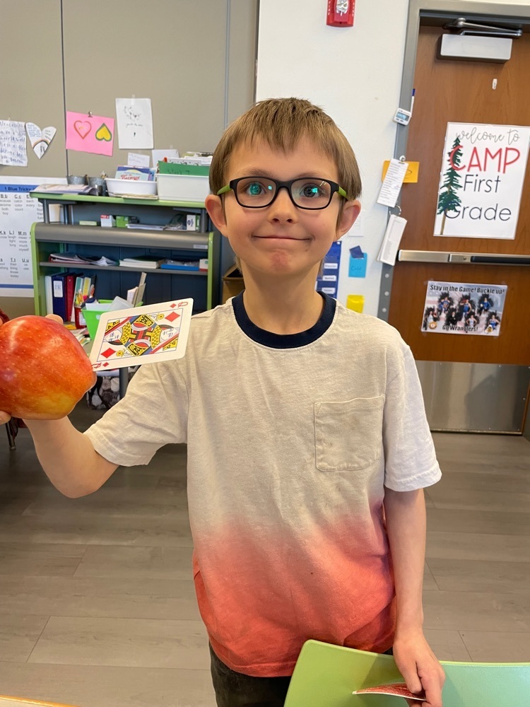 Student holding an apple with a card stuck in it. 