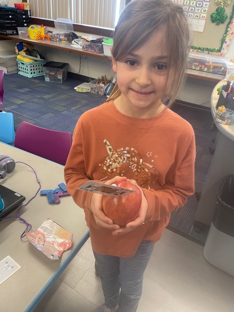 Student holding an apple with a card stuck in it.